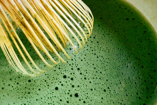 Bamboo whisk mixing vibrant green matcha tea with bubbles in a bowl