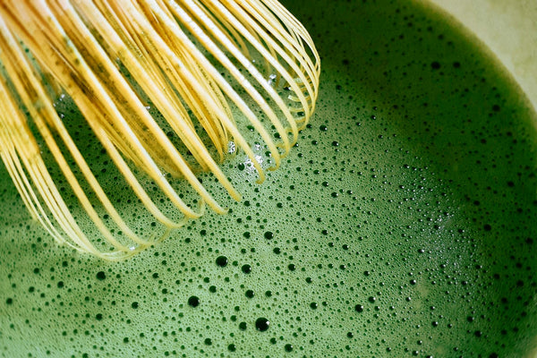 Bamboo whisk mixing vibrant green matcha tea with bubbles in a bowl
