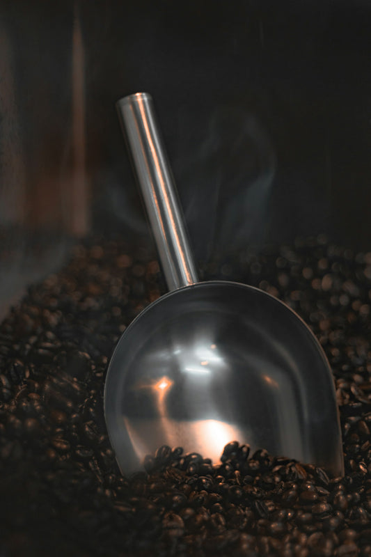 A metal scoop resting on a pile of roasted coffee beans